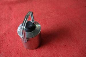 Silver thermos with a black lid on a red surface. photo