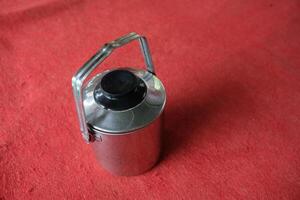 Stainless steel container with black lid and handle on red surface. photo