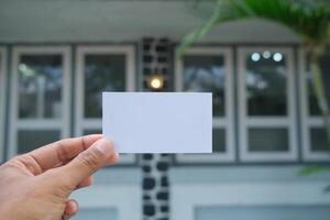 Hand holding blank white card against blurred house background. photo