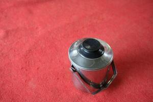 Silver container with black lid on red surface. photo