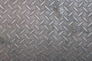 Close-up of textured metal surface with diamond pattern and a single screw. photo