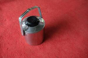 Stainless steel thermos with a black lid and handle on a red background. photo