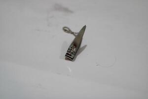 A single, silver nail clipper with a chain sits on a white surface. photo