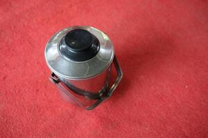 Stainless steel kettle with black lid on red surface. photo