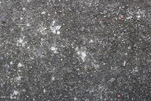 Closeup of rough, textured concrete surface with small stones and white patches. photo