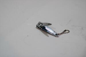 A silver nail clipper with a chain lies on a white surface. photo