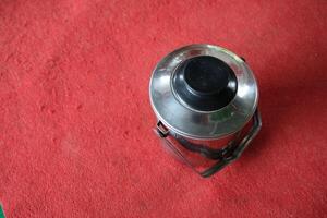 A stainless steel container with a black lid on a red surface. photo