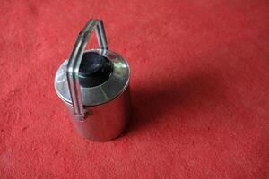 Stainless steel container with handle on red surface. photo