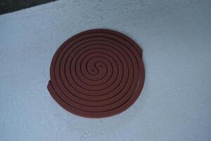 A single brown mosquito coil on a white surface. photo