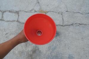 A red plastic funnel held in a hand, against a cracked grey concrete background. photo