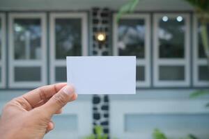 Hand holding a blank white card against a blurred background of a building. photo