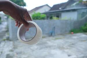 Close-up of a hand holding a roll of clear packing tape. photo