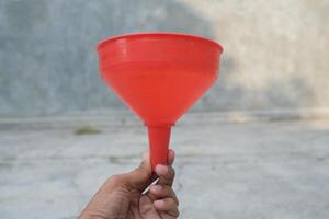 Red plastic funnel held by hand against a blurred background. photo