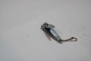A silver nail clipper with a chain lies on a white surface. photo