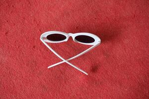 White oval sunglasses on red surface. photo