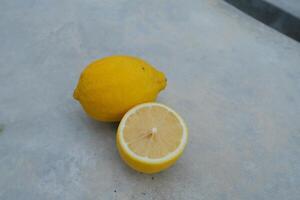 A whole lemon and a sliced lemon on a grey surface. photo