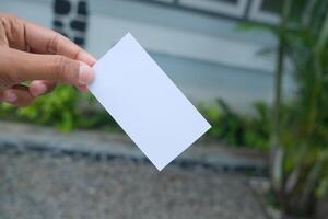 Hand holding a blank white card with a blurry background. photo
