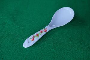 White spoon with floral design on a green surface. photo