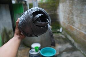 A hand holds a ball of black twine, with a blue basin out of focus. photo