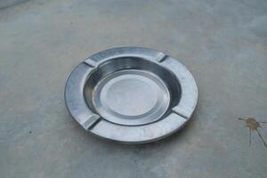 A silver metal ashtray sits on a grey concrete surface. photo