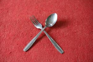 A fork and spoon crossed on a red surface. photo