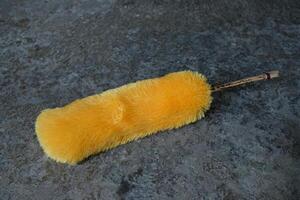 A yellow duster with a wooden handle lies on a concrete surface. photo
