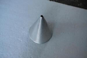 A single, metallic, cone-shaped mold sits on a white surface. photo