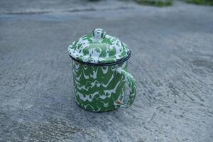 Green and white enamel mug with lid on a concrete surface. photo