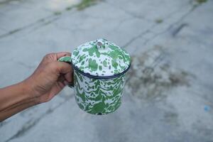 Hand holding a green and white patterned mug with a lid. photo