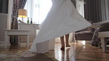 The bride goes to the window in a white robe. A bride in a flowing white gown twirls gracefully in a beautifully decorated room, with soft light streaming through the window. video