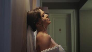 Bride Leaning Against Wall with a Content Smile. A bride leans back against a wall, her face lit with a content smile as she enjoys a quiet moment before the wedding. video