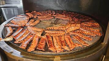 Barbecue ribs cooking on a circular smoker grill. A large circular smoker grill filled with rows of barbecue ribs sizzling over a fire. video