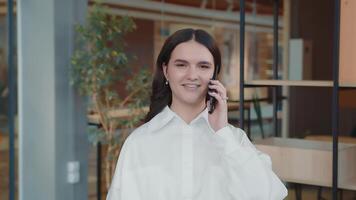 Portrait of a young girl yak in the office talking on the phone, laughing and wondering at the camera. A young student speaks on the mobile. video