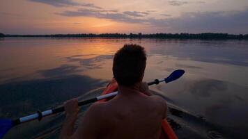 A man kayaks on a calm river towards the sunset. He skillfully rowing oar. Beautiful nature of the evening river. Super Slow Motion video