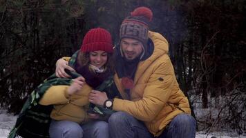Guy shelters a girl with a blanket in the winter forest. Tourists travel together. They are smiling and happy. Travel and adventure concept. video