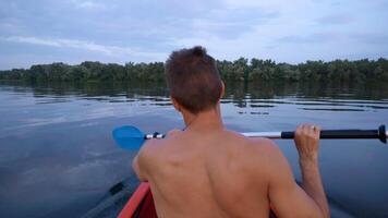 A man kayaks on a calm river. He skillfully rowing oar. Beautiful nature of the evening river. Super Slow Motion video