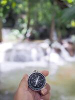 Close up of compass in woman hand with waterfall as background. The concept of world tourism day, Searching the right directions and Travel photo