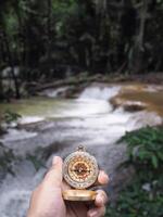 Close up of compass in woman hand with waterfall as background. The concept of world tourism day, Searching the right directions and Travel photo