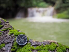 Compass on the rock with waterfall as background. The concept of world tourism day, Searching the right directions and Travel photo