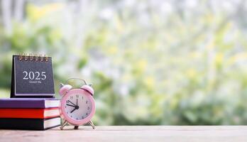 Student creative desktop, 2025 desk calendar on hardcover book and pink alarm clock. Copy space for text, Back to school, Education concept photo