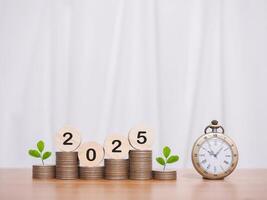 Vintage watch, Wooden blocks with the number 2025 and plants growing up on stack of coins. The concept of saving money for manage time to success business in year 2025 photo
