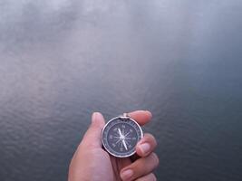Close up of compass in woman hand with water as background. The concept of world tourism day, Searching the right directions and Travel photo