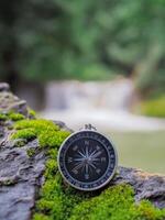 Compass on the rock with waterfall as background. The concept of world tourism day, Searching the right directions and Travel photo