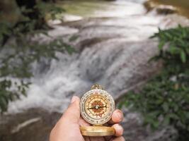 Close up of compass in woman hand with waterfall as background. The concept of world tourism day, Searching the right directions and Travel photo