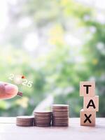Close up hand putting coin into stack of coins and Wooden blocks with the word TAX. The concept about saving money and manage time to paying tax photo