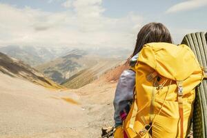 Close up view from the back unrecognizable woman with yellow stylish backpack with flask sticking out of the side pocket. Mock up copy space banner. Woman watch mountains valley in sunny day photo