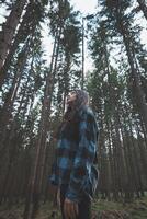 Happy woman in a plaid shirt enjoying the serenity of a dense forest, surrounded by tall trees, feeling freedom and connection with nature photo