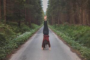 Acrobatic woman in black leggings and plaid shirt performs a cartwheel on a forest path in the middle of a deep forest. Coordination and agility training photo