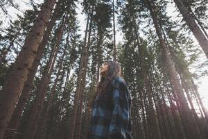 Happy woman in a plaid shirt enjoying the serenity of a dense forest, surrounded by tall trees, feeling freedom and connection with nature photo