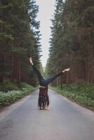 Acrobatic woman in black leggings and plaid shirt performs a cartwheel on a forest path in the middle of a deep forest. Coordination and agility training photo